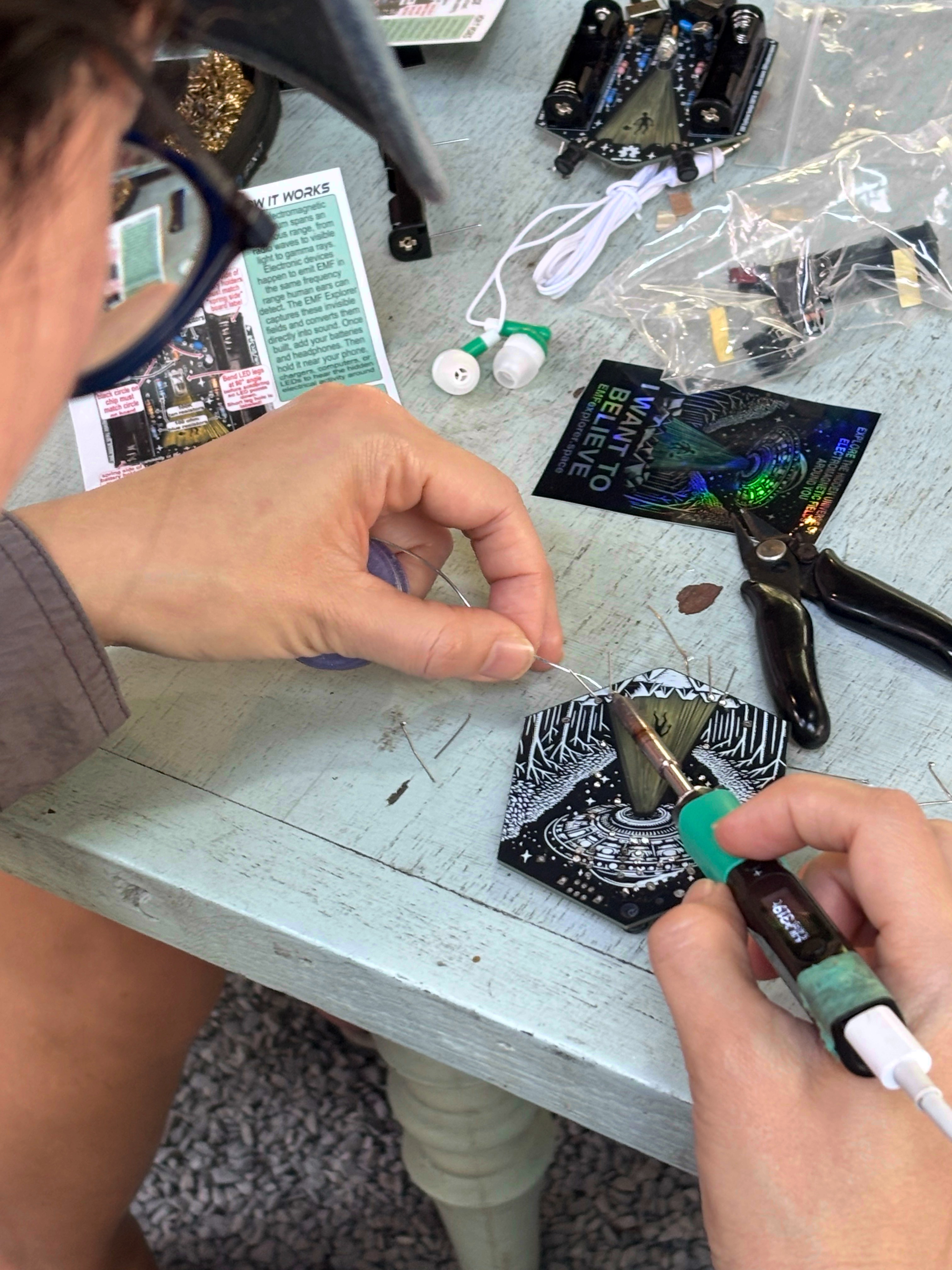Participant soldering an EMF Explorer badge at a workshop table