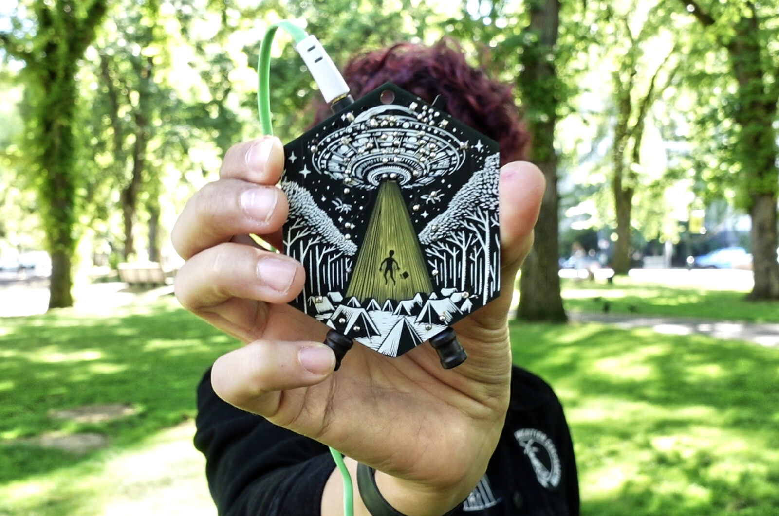 Holding the EMF Explorer badge outdoors in a park